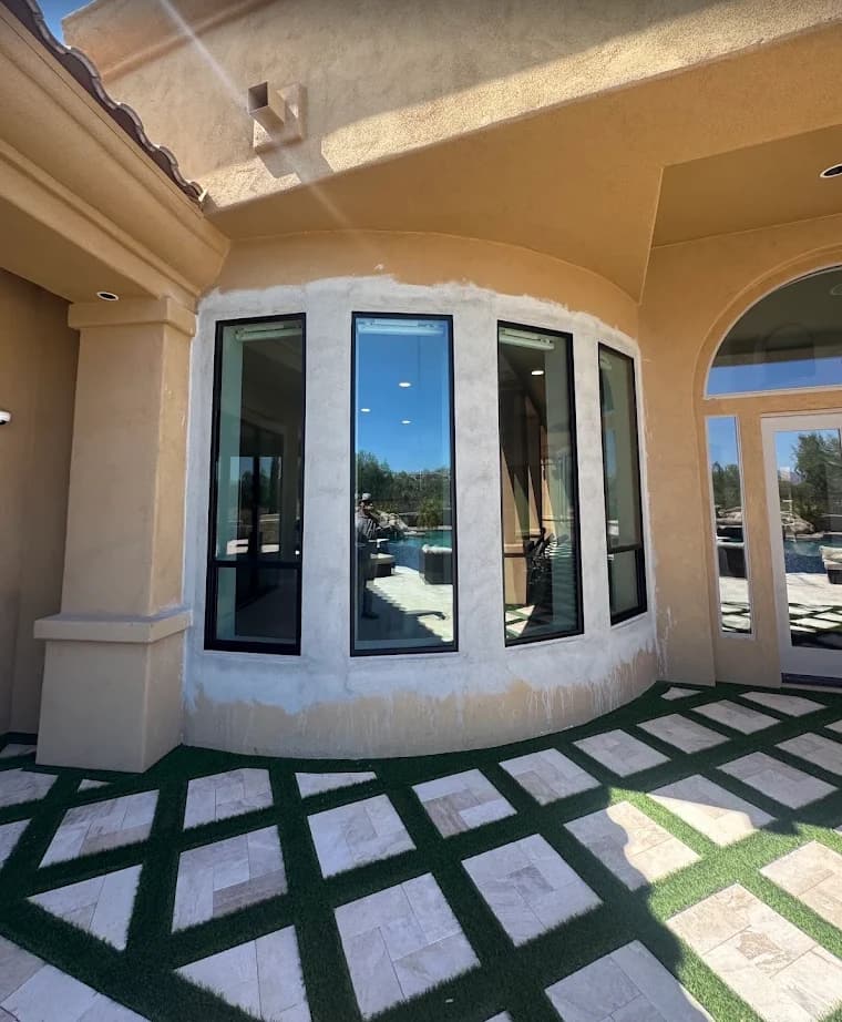 Curved bay of tall windows with fresh base coat stucco around the openings on a tan stucco home